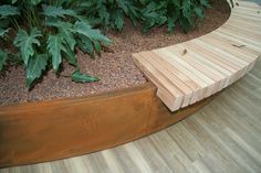 a wooden bench sitting on top of a hard wood floor next to green plants and trees