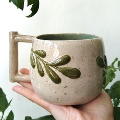 a hand holding a ceramic mug with leaves on it