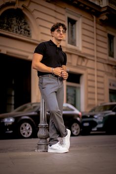 a man leaning on a pole in front of a building with cars parked outside it