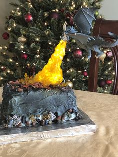 there is a cake that looks like a dragon on top of a table next to a christmas tree