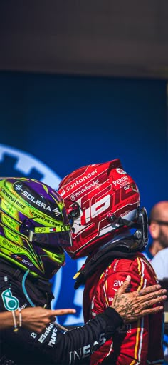 two men in racing gear standing next to each other with their hands on the back of their heads