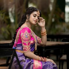 a woman in a pink and purple sari sitting at a table with her hand on her face