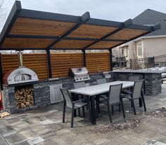 an outdoor kitchen with grill and dining table in the foreground, next to a fire pit