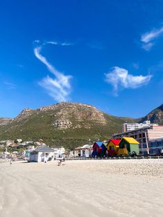 colorful beach huts line the shore of a sandy beach with mountains in the back ground