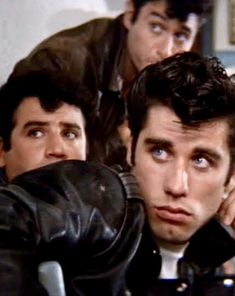 three men in leather jackets looking at the camera with one man holding his hand up to his ear