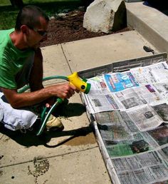 a man sitting on the sidewalk with a hose in his hand spraying water onto newspapers