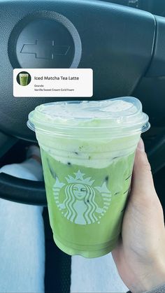 a person holding up a starbucks drink in their hand while sitting in the driver's seat of a car