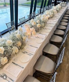 a long table is set with white flowers and place settings for the guests to sit at