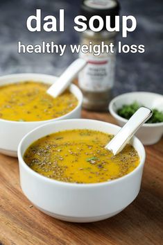 two white bowls filled with soup on top of a wooden cutting board