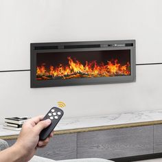 a person is holding a remote control in front of a fireplace that has flames on it