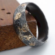 a black and gold ring sitting on top of a piece of wood