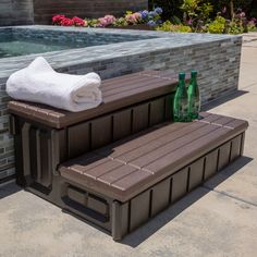 two brown benches sitting next to each other near a swimming pool with towels on it