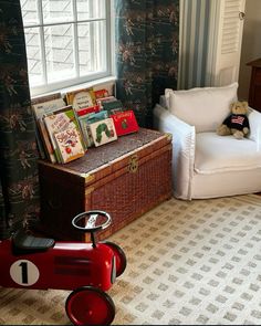 a toy car sitting in front of a window next to a chair and bookshelf