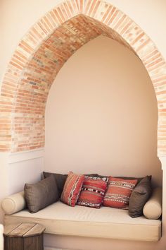 a white couch sitting under an arched window next to a wooden table with two pillows on it