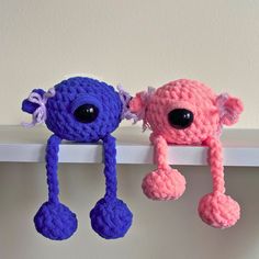 two crocheted toys are hanging on the wall, one pink and one blue