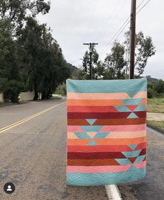 a colorful quilt sitting on the side of a road next to a street sign and telephone pole