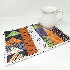 a white cup sitting on top of a table next to a mug mat with halloween designs