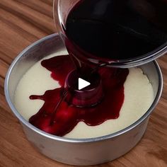 a person pouring red liquid into a metal container on top of a wooden table,