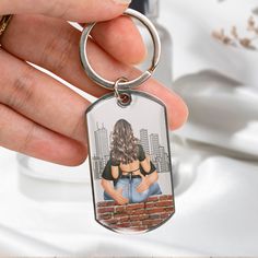 a hand holding a keychain with a picture of a woman on the brick wall