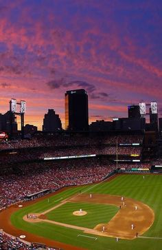 a baseball stadium filled with lots of people watching the sun go down in the distance