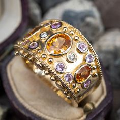 This wonderful wide band cocktail ring is accented with three (3), bezel set, oval mixed cut natural spessartite garnets, twelve (12), bezel set, round brilliant cut natural pink sapphires and six (6), bezel set, round brilliant cut diamonds. The ring measures 17.0mm at the top, rises 5.8mm above the finger, tapering to 4.9mm wide and 1.1mm thick at the base of the shank. This ring is currently a size 10. Wide Band Diamond Rings, Purple Garnet, Spessartine Garnet, Gemstone Wedding Rings, Multicolor Jewelry, Spessartite Garnet, Wide Band Ring, Wide Band Rings, Rocks And Gems