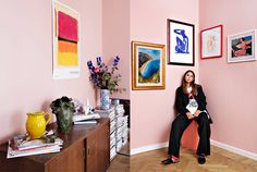 a woman sitting on a chair in front of a wall with pictures and vases