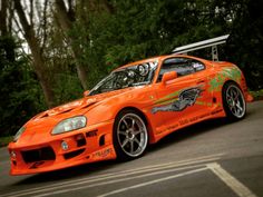 an orange sports car is parked on the side of the road in front of some trees