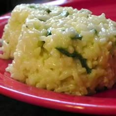 a red plate topped with rice and vegetables on top of a black table next to a cup