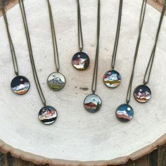 six necklaces with mountains on them sitting on a tree stump