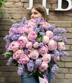 a woman holding a bouquet of pink and purple flowers in front of a brick wall