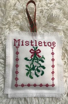 a cross stitch christmas ornament hanging on a white furnishing with a red ribbon