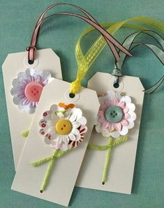 three tags with flowers on them are hanging from a green ribbon and one has a button in the middle