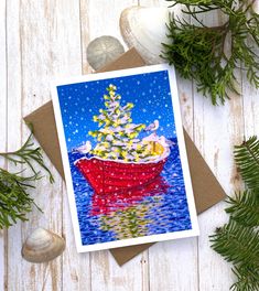 a card with a christmas tree on it sitting next to some sea shells and pine branches