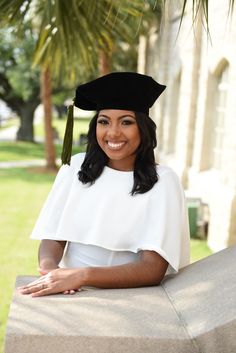 a woman wearing a graduation cap and gown sitting on a bench in front of a palm tree