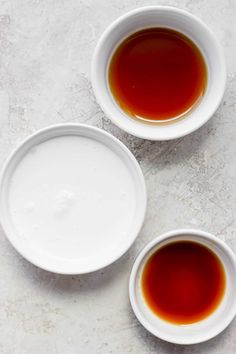 three white bowls filled with liquid sitting on top of a table