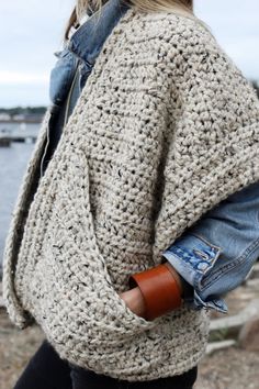 a woman wearing a crochet sweater and leather wristbands is standing by the water