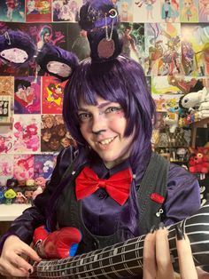 a woman with purple hair and bunny ears holding a guitar in front of a wall full of pictures