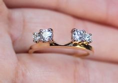 a close up of a person's hand holding a gold ring with two diamonds