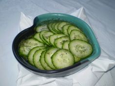 a bowl filled with cucumbers sitting on top of a white cloth covered table