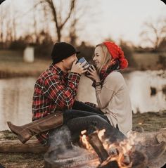 a man and woman sitting next to a campfire drinking coffee