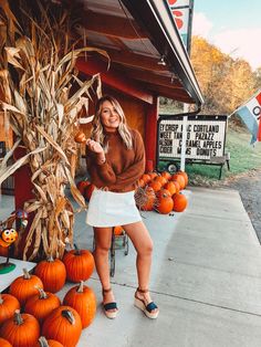 a woman standing in front of a store with pumpkins and corn on the cob