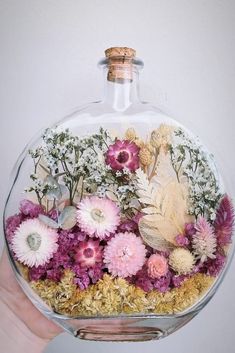 a hand holding a glass bottle filled with flowers and plants in it's bottom