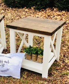 two small wooden tables with plants in them on the ground next to a pillow and some leaves