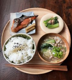 a wooden plate topped with rice, meat and veggies next to chopsticks