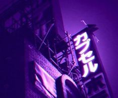 a neon sign on the side of a tall building in purple hued lighting,