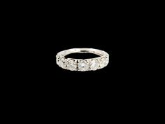 a white gold ring with three diamonds on the top and bottom, against a black background