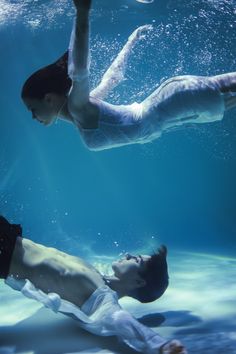 two people are swimming under the water in an underwater pool and one person is holding his leg up