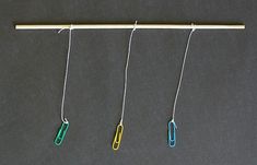 three different colored paper clips hanging from a clothes line on a black surface with a pencil