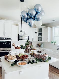 a kitchen filled with lots of food on top of a white counter topped with balloons