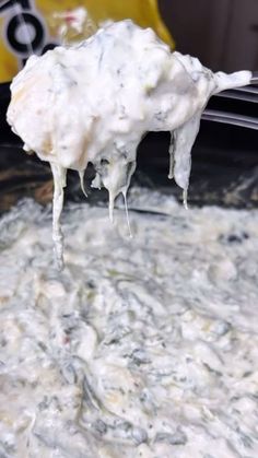 a spoon full of food is being lifted from the crock pot with white sauce